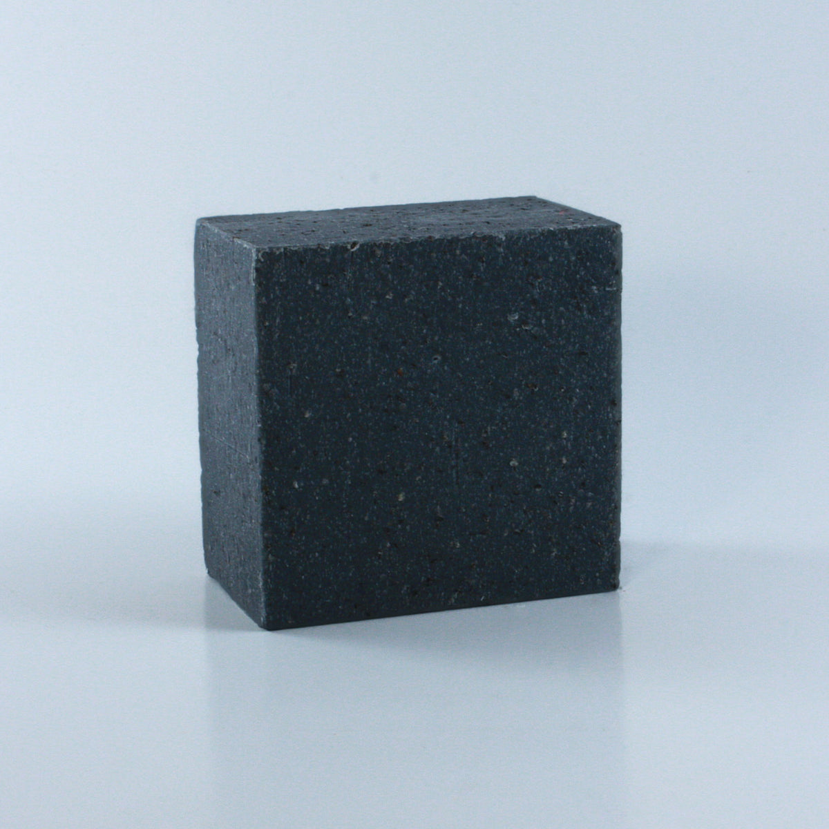 Concrete + Clay Unscented Exfoliating Hand Soap with a black speckled and heavily textured finish and clean rectangular shape photographed from an angle on a neutral background.