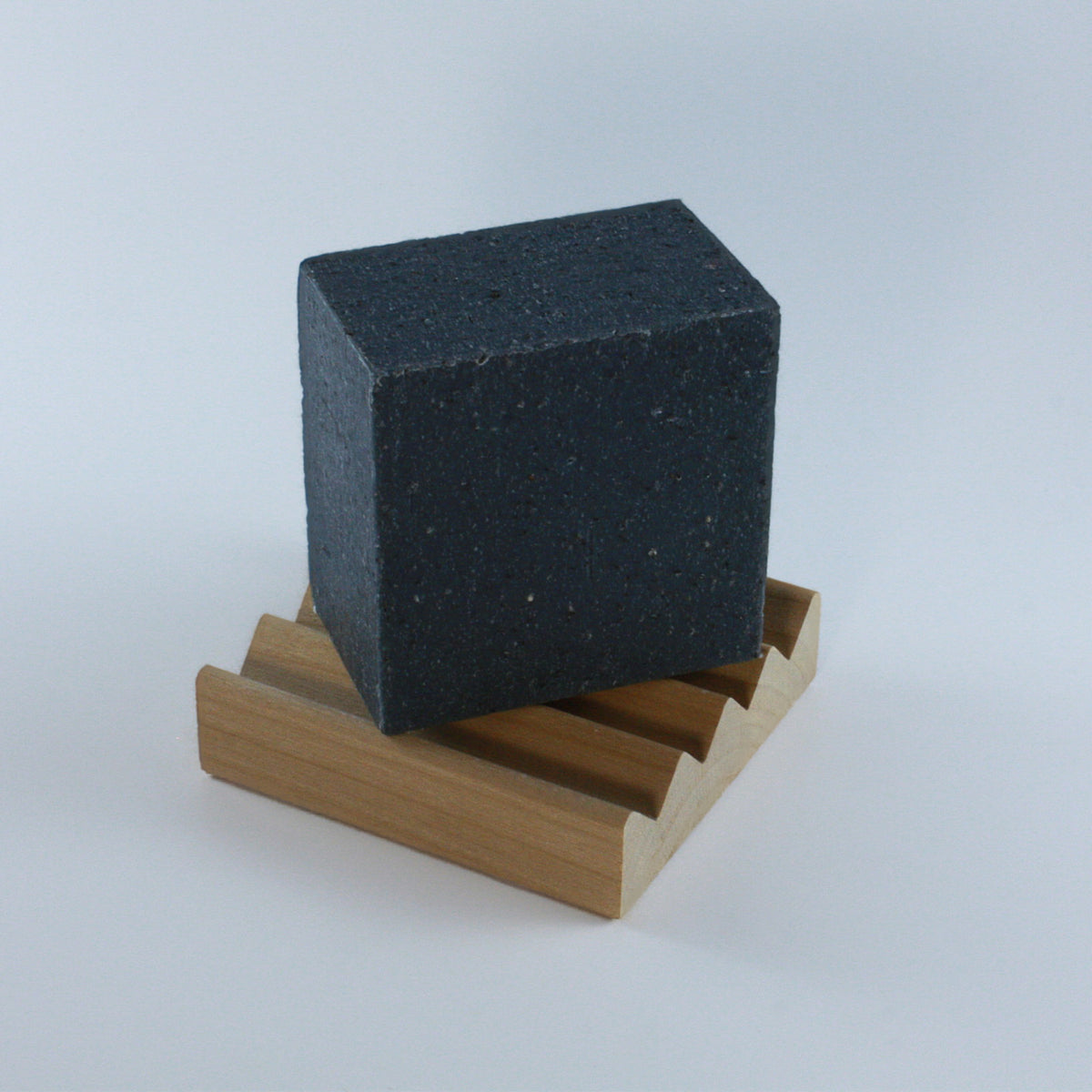 Wooden Soap Rest holding a handcrafted black soap bar photographed at an angle on neutral background